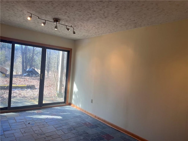 empty room with baseboards, a textured ceiling, and track lighting