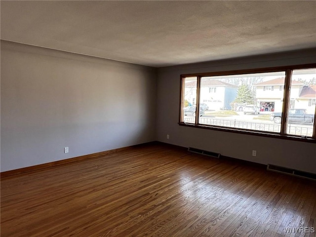 empty room with baseboards, visible vents, and dark wood-style flooring