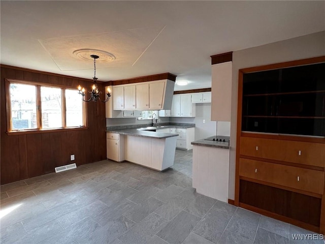 kitchen featuring visible vents, black electric stovetop, a peninsula, an inviting chandelier, and white cabinets