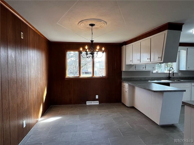 kitchen with dark countertops, wooden walls, a notable chandelier, white cabinetry, and a sink