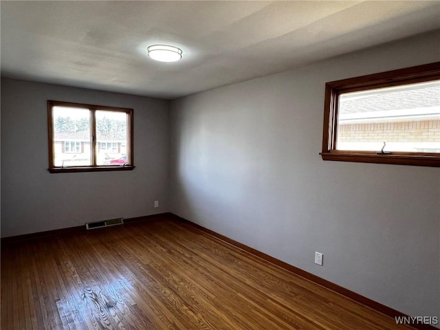 spare room featuring visible vents, baseboards, and dark wood-style floors