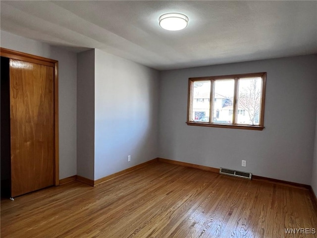 empty room with visible vents, light wood-style flooring, and baseboards