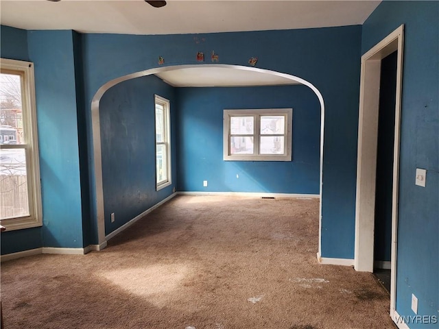 empty room with carpet, baseboards, and arched walkways