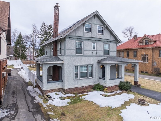 view of front of house with stucco siding, a porch, a chimney, and fence