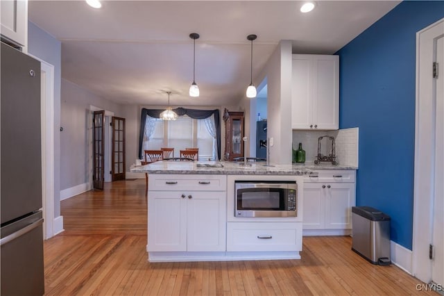 kitchen with a peninsula, stainless steel appliances, decorative backsplash, white cabinets, and light wood-type flooring