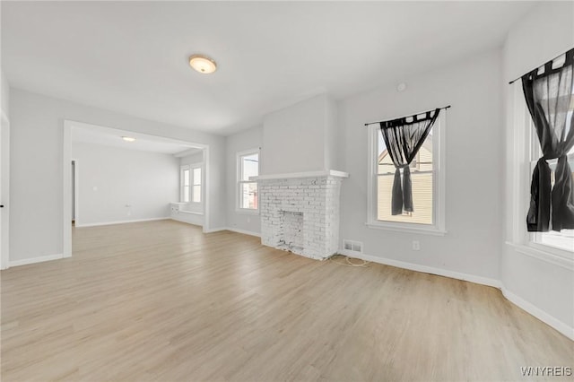 unfurnished living room with visible vents, light wood-style flooring, a brick fireplace, and baseboards