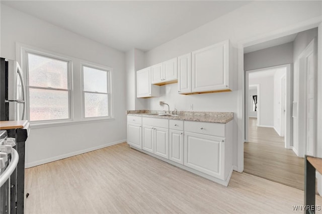 kitchen featuring white cabinetry, light wood-type flooring, freestanding refrigerator, and a sink