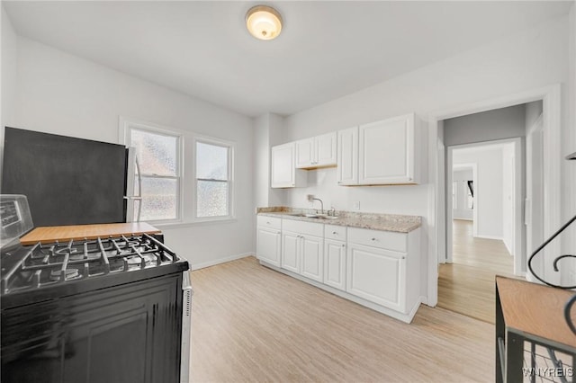 kitchen featuring gas range, white cabinetry, light wood-style flooring, and a sink