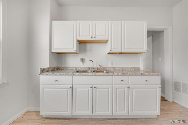 kitchen with visible vents, baseboards, light wood-type flooring, white cabinetry, and a sink