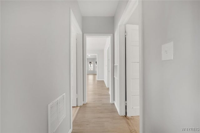 hall with light wood-style floors, visible vents, and baseboards