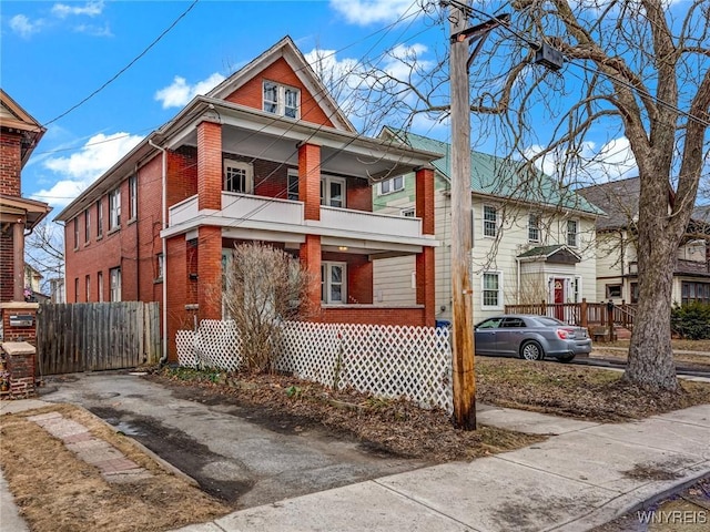 view of front of house featuring brick siding, a balcony, driveway, and fence