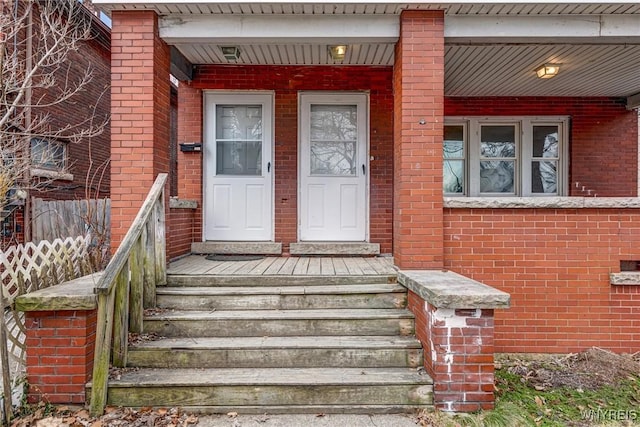 view of exterior entry featuring brick siding and a porch