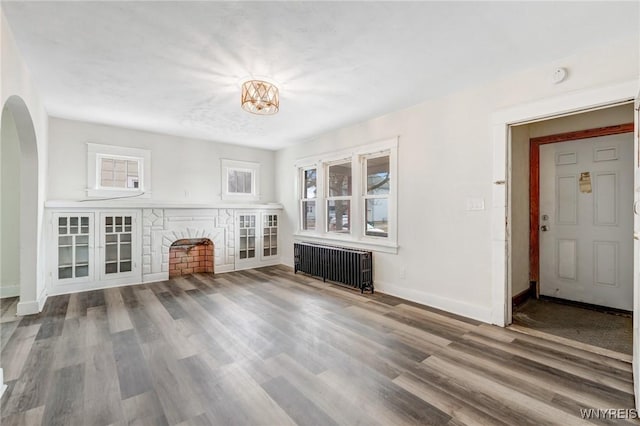 unfurnished living room with baseboards, radiator, wood finished floors, and arched walkways