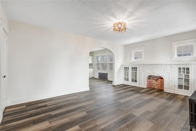 unfurnished living room featuring radiator, wood finished floors, arched walkways, and baseboards