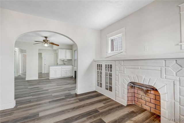 unfurnished living room featuring baseboards, wood finished floors, arched walkways, and ceiling fan