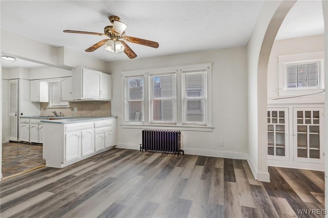 kitchen featuring radiator heating unit, arched walkways, a peninsula, white cabinets, and dark wood-style flooring