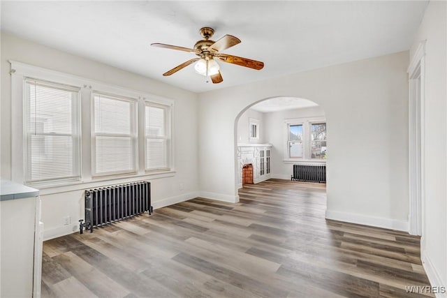 unfurnished living room with radiator, wood finished floors, arched walkways, and baseboards