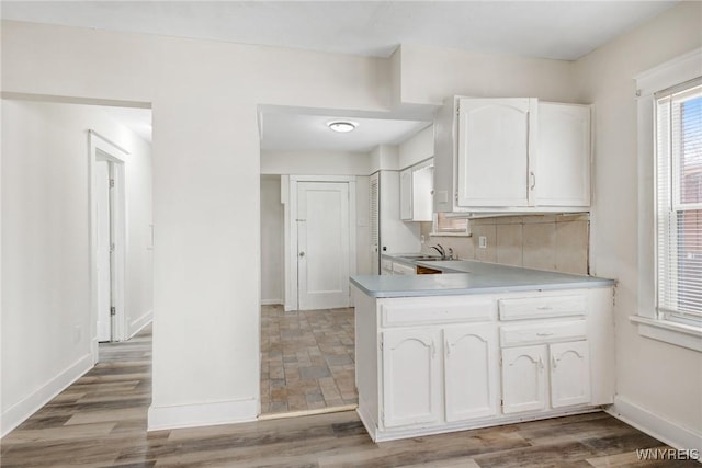 kitchen with white cabinetry, baseboards, light wood finished floors, and a sink