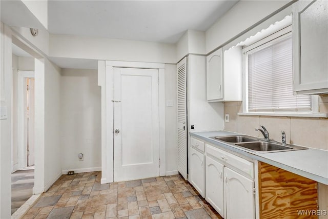 kitchen with baseboards, a sink, light countertops, stone finish flooring, and white cabinetry