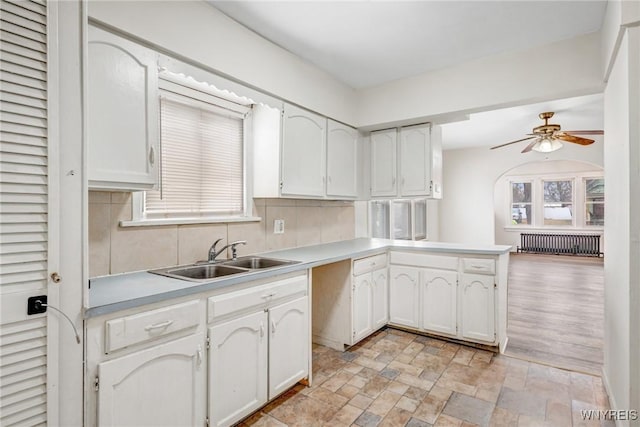 kitchen featuring decorative backsplash, white cabinets, radiator, and a sink