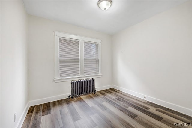 spare room featuring radiator, wood finished floors, and baseboards