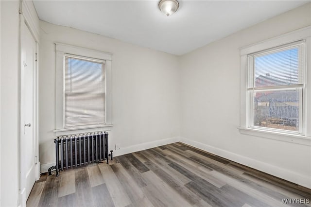 unfurnished room featuring radiator heating unit, baseboards, and wood finished floors