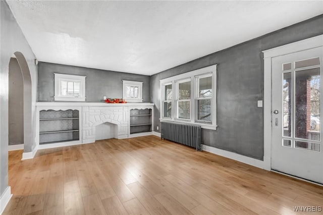 unfurnished living room with baseboards, arched walkways, radiator heating unit, and light wood finished floors