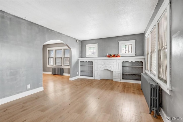 unfurnished living room with arched walkways, radiator, baseboards, and wood finished floors