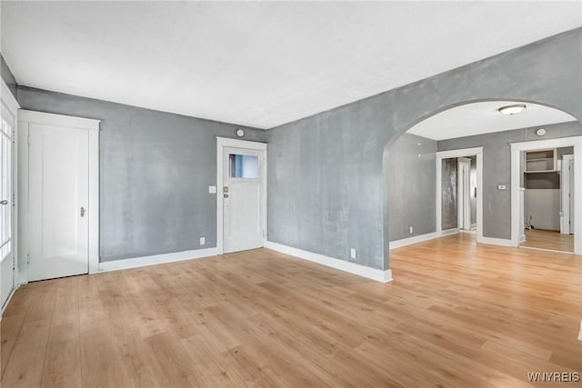 spare room with baseboards, arched walkways, and light wood-style flooring