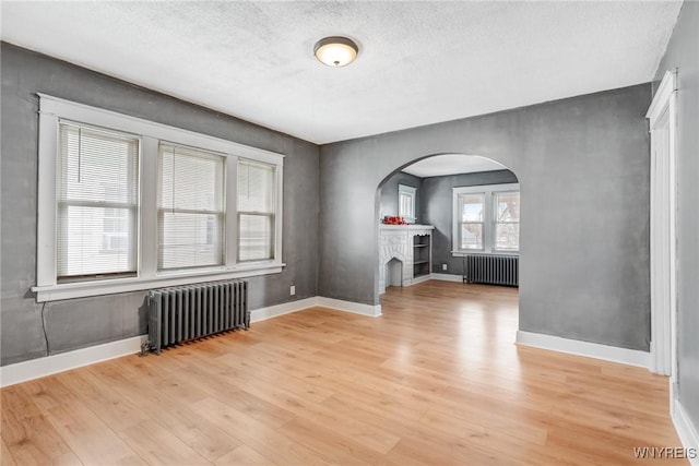 unfurnished living room with arched walkways, radiator, and light wood-style flooring