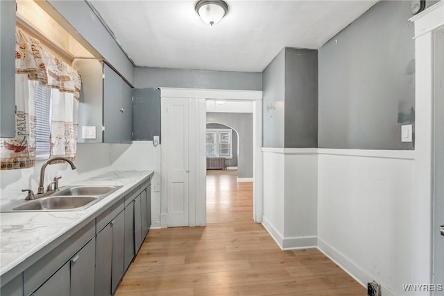 kitchen featuring arched walkways, light wood finished floors, gray cabinetry, and a sink