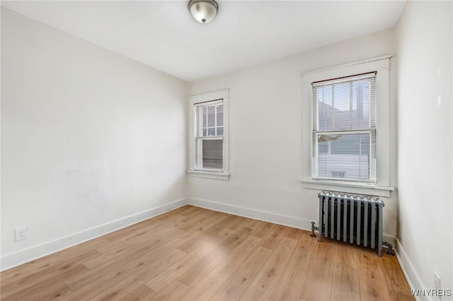 spare room featuring radiator, baseboards, and light wood-style floors