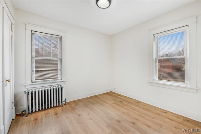 empty room with baseboards, radiator heating unit, and light wood finished floors