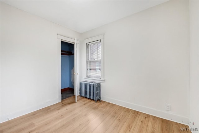 unfurnished bedroom featuring a closet, radiator heating unit, baseboards, and light wood finished floors