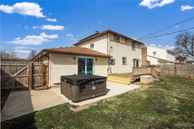 rear view of property featuring a gate, fence, a hot tub, a patio area, and a lawn