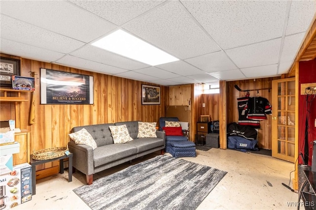 living area with a drop ceiling, wooden walls, and concrete floors