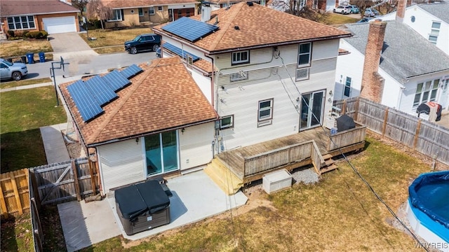 rear view of property with a deck, solar panels, a fenced backyard, and a shingled roof