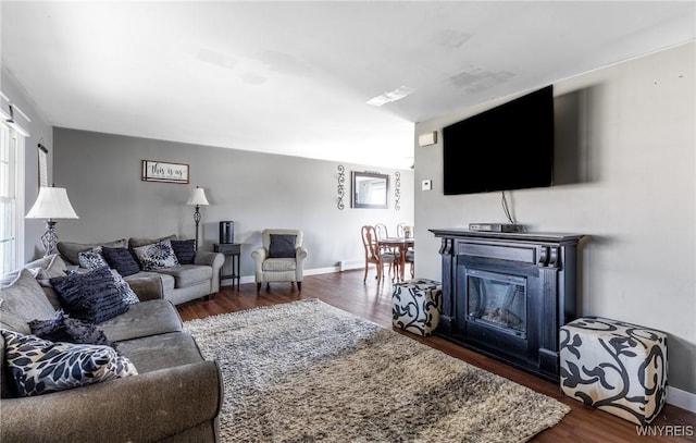 living room with baseboards, dark wood-type flooring, and a glass covered fireplace