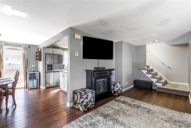 living area featuring beverage cooler, a glass covered fireplace, dark wood finished floors, stairway, and baseboards