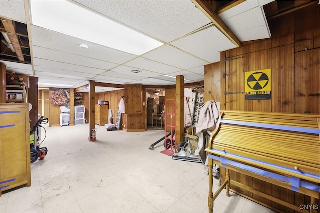 finished basement featuring tile patterned floors, wooden walls, and a drop ceiling