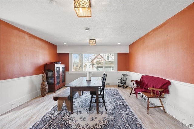 dining space with a wainscoted wall, a textured ceiling, and wood finished floors