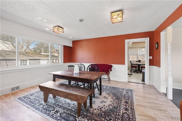 dining room featuring light wood-style flooring, wainscoting, visible vents, and a textured ceiling