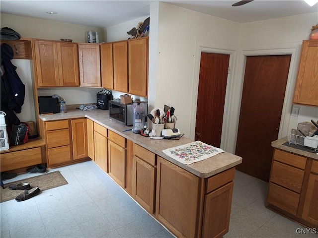 kitchen with stainless steel microwave, light floors, a peninsula, and light countertops