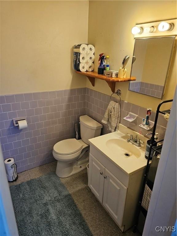 half bathroom featuring tile walls, toilet, wainscoting, tile patterned floors, and vanity