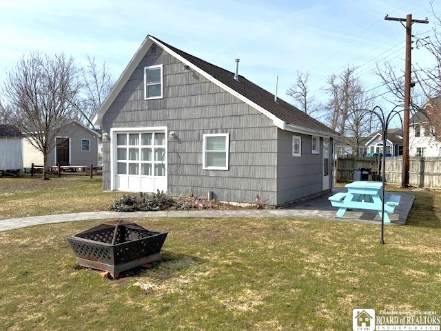 view of side of property featuring fence, a fire pit, and a lawn