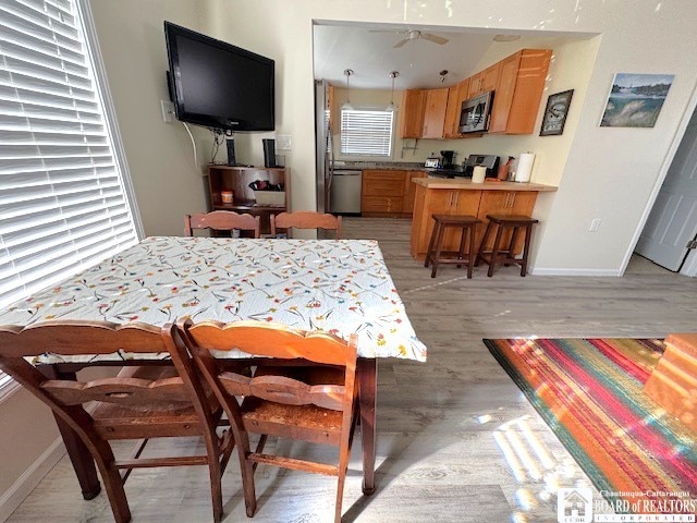 dining space featuring light wood finished floors, baseboards, and a ceiling fan