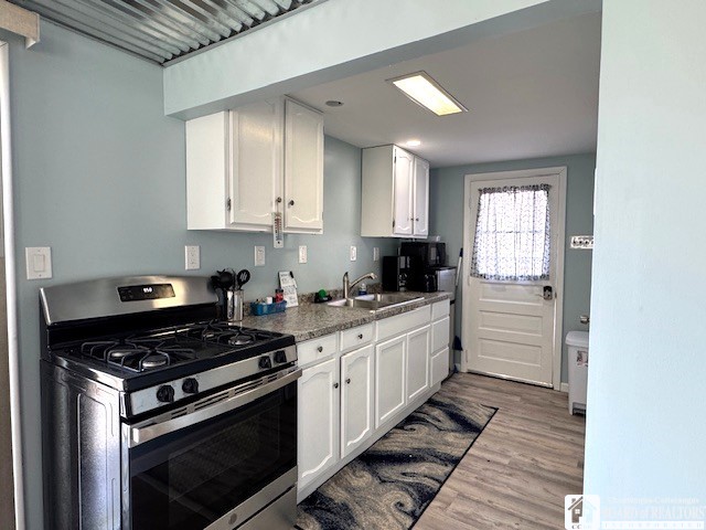 kitchen featuring a sink, gas range, white cabinets, and wood finished floors