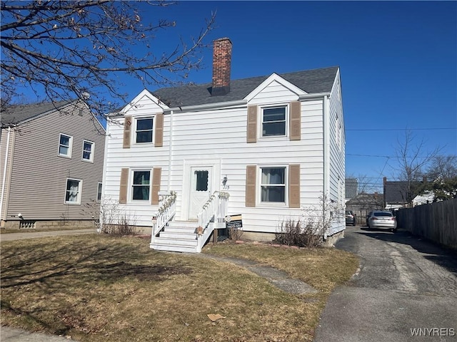 view of front of house featuring a front yard, fence, roof with shingles, a chimney, and aphalt driveway