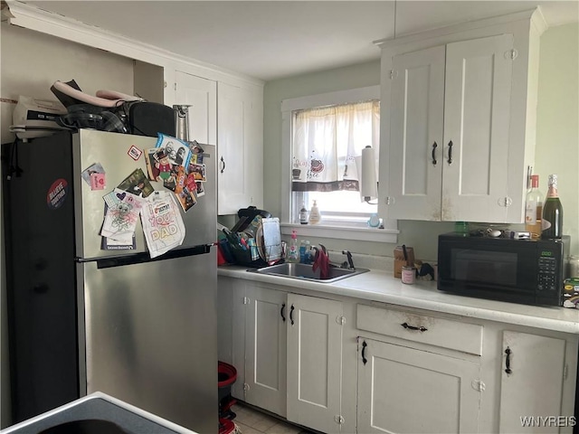 kitchen featuring a sink, white cabinetry, freestanding refrigerator, black microwave, and light countertops