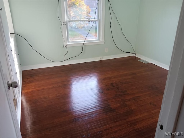 spare room featuring dark wood-style floors, visible vents, and baseboards